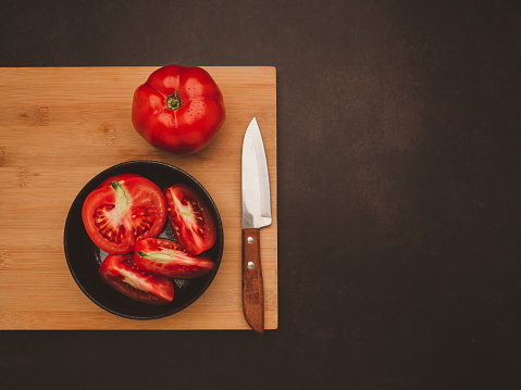 Fresh tomatoes on a wooden cutting board with a knife on a vintage background. Harvesting tomatoes. Top view. Close-up photo. Space for text. Health foods concept