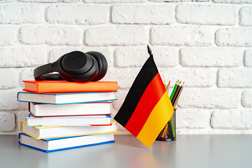 Stack of books and flag of Germany on desk. German language learning concept