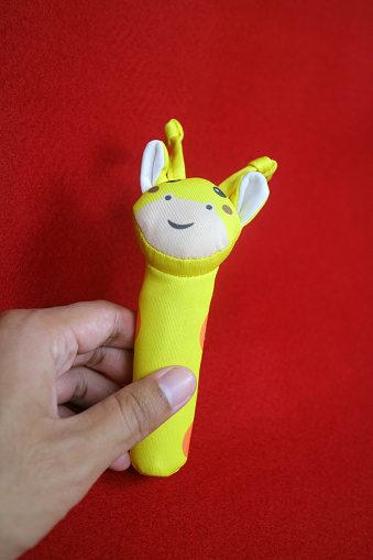 A hand holding yellow giraffe shaped baby holding toy that makes a sound when squeezed. on a red background