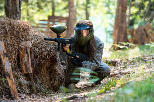 paintball sport player in protective uniform and mask aiming gun before shooting