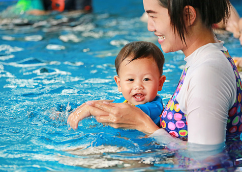 Happy family of mom teaching baby boy in swimming pool