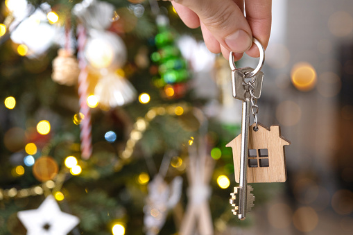 Key to the house with a keychain is hanging on the Christmas tree. A gift for New Year, Christmas. Building, design, project, moving, insurance, mortgage, rent and purchase real estate. Copy space