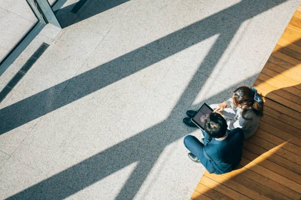 From a high angle view, two businesspersons are seated on chairs in the lobby discussing business matters.