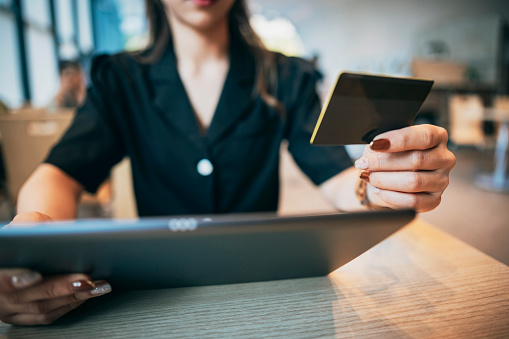 At a coffee shop, a businessperson is using a credit card to pay for an online purchase. They might be seated at a coffee table, holding a smartphone or a laptop, conducting an online transaction.