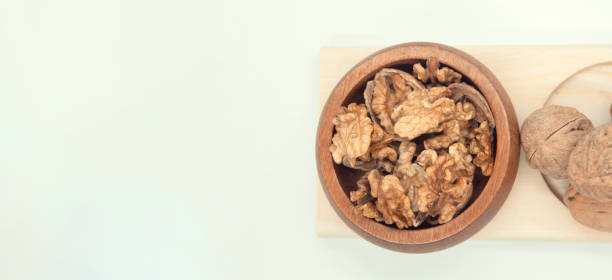 istock Walnut kernel halves, in a wooden bowl on white background. Close-up 1801793857