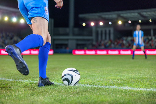 Female soccer player doing kick off during sports match, legs medium shot