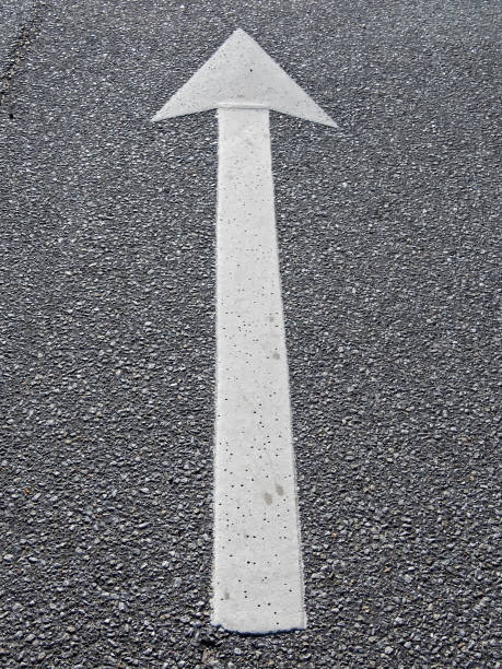 A white arrow on black asphalt pointing straight ahead