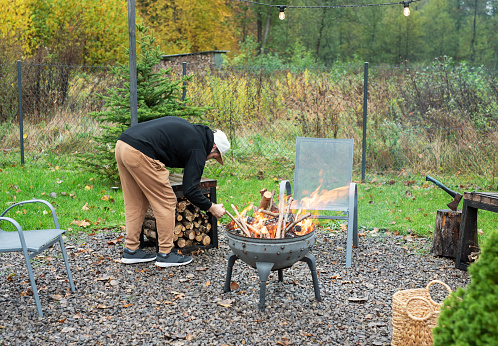 A man lights a barbecue in nature near the house
