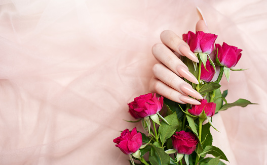 Elegant pastel pink natural manicure. Female hands  with roses on pink silk background.