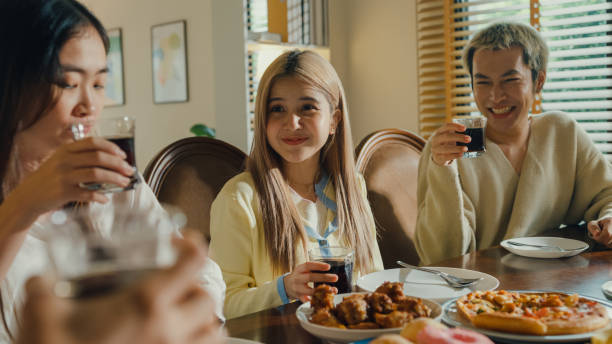 istock Group of young Asian people drinking cola and having fun sitting at dining table at home. Multicultural friends having fun together college house party. 1801866976