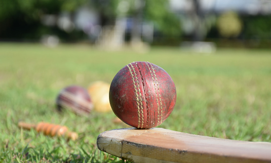 Old leather cricket balls and cricket sportwears on the green grass lawn, concept for practicing cricket sports.