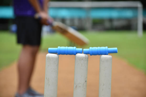 Male cricket coach holds helmet and bat in the green grass court of school before teaching cricket sport to students at school in the afternoon of the day.