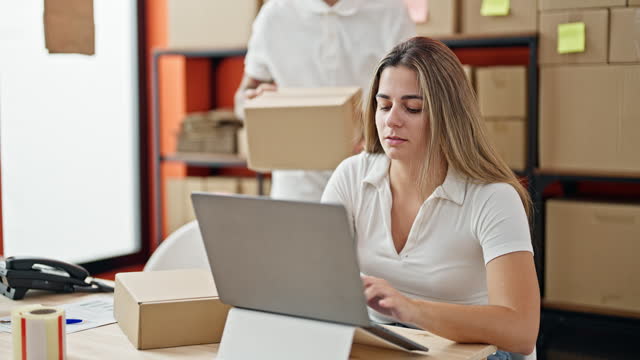 Two workers man and woman using laptop checking package at office