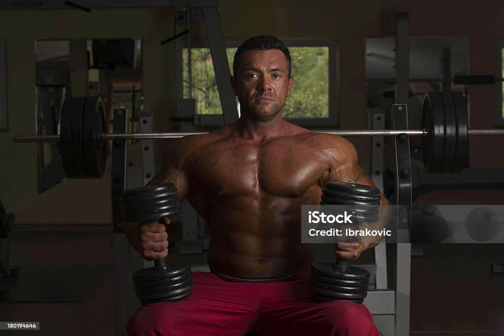 Tronco Nu body builder posando com halteres no banco - Foto de stock de Academia de ginástica royalty-free