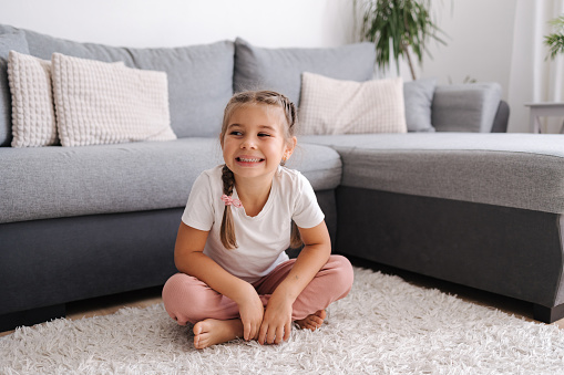 Active and energetic little girl have fun and home. Living room. Kid sitting on the carpet.