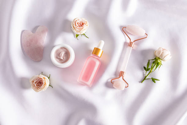 istock Cosmetic massage tools and self-care products on white delicate satin with fresh rose buds. Top view. Flat layout. home care. 1801959480