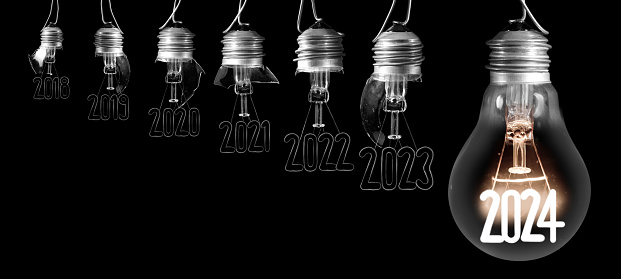 Horizontal group of shining light bulb with fiber in a shape of New Year 2024 and broken light bulbs with years passed isolated on black background.
