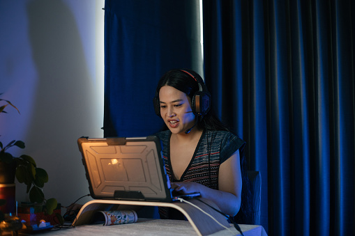Nightime portrait of woman at computer with headset on and developing software during conference with neon lighting.