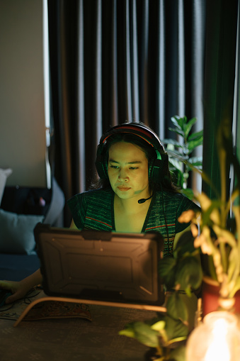 A woman at home on her laptop in her dark and cosy living room while her face is illuminated by the green color from her laptop screen.