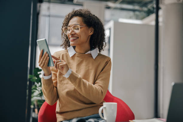 istock Smiling business woman is using mobile phone while sitting in office during break time 1802010112