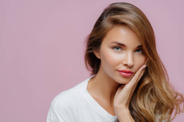 istock Graceful woman with hand on face, wavy hair, in a white tee, with a thoughtful expression 1802019331