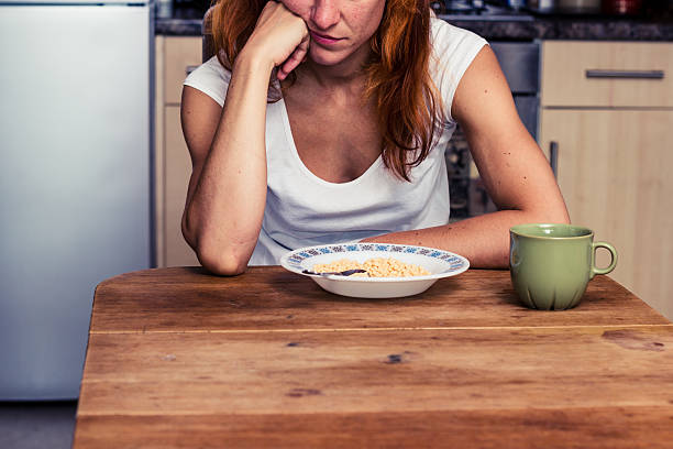 Woman doesn't want to eat her cereal Young woman in her kitchen is dissapointed that she is having cereal for breakfast again dyed red hair photos stock pictures, royalty-free photos & images
