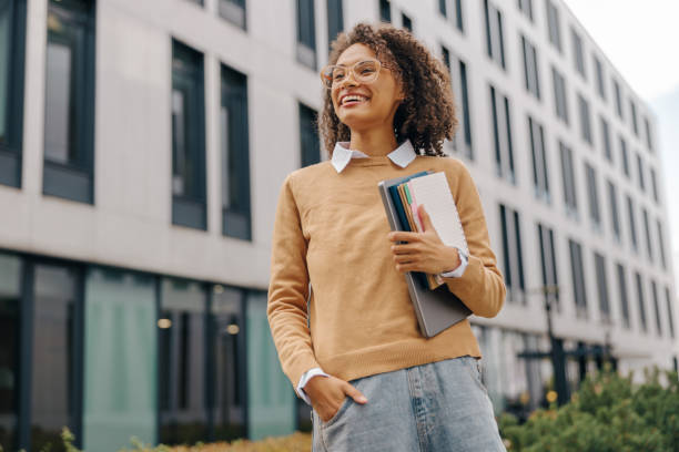istock Smiling female freelancer standing with laptop and note pads on modern building backgrounds 1802038307