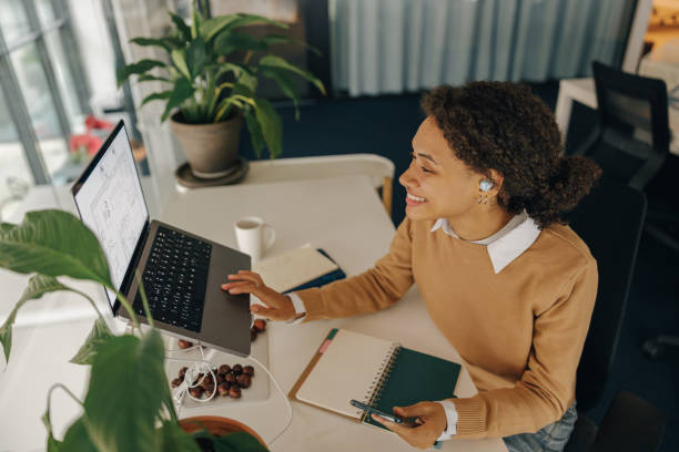 istock Smiling business woman working on project while use laptop and making notes in office 1802048356