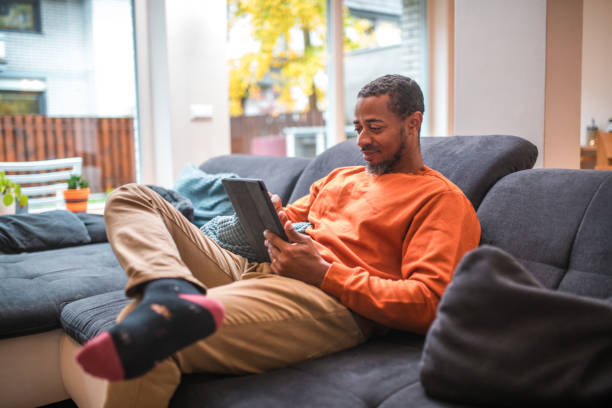 istock Mid Adult Black Male on Sofa with Digital Tablet 1802052023