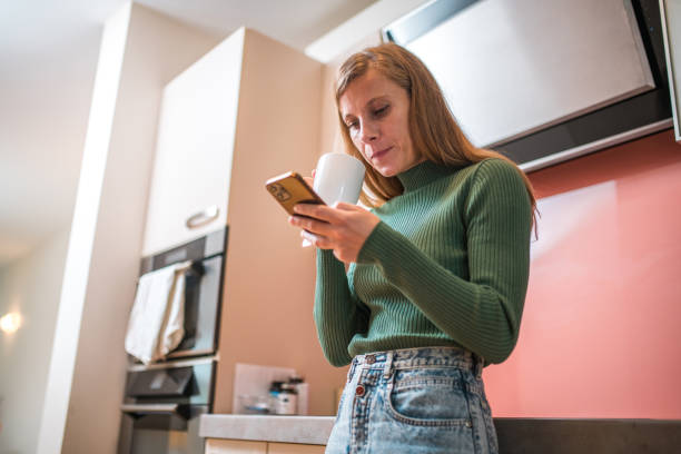 istock Mid Adult Caucasian Female in Kitchen Using Smartphone 1802052585