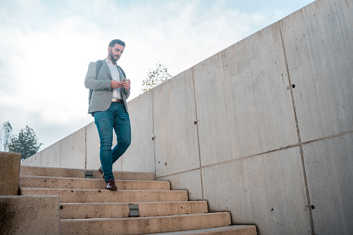 A Caucasian male using his smartphone for online banking while walking down the stairs outdoors.