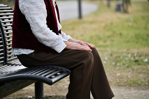 Elderly Japanese woman sitting on a bench in the park and looking at fresh greenery