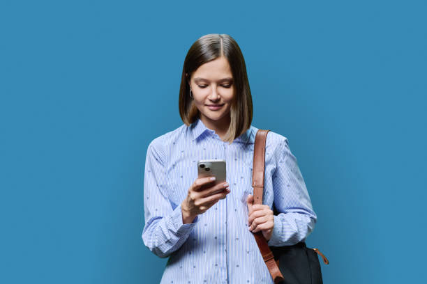 istock Young woman student with smartphone backpack on blue studio background 1802088199