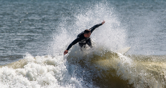 Gilgo Beach, New York, USA - 31 August 2023: A man riding a wave on top of a surfboard and falling.