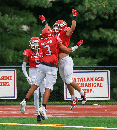 West Islip, New York, USA - 16 September 2023: Two high school football players jumping in the air for a chest bump after scoring a touchdown during a game.