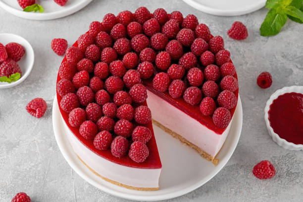 No baked raspberry cheesecake or raspberry cream mousse cake with jelly and fresh berries on top on a white plate on a gray concrete background. Summer cake.