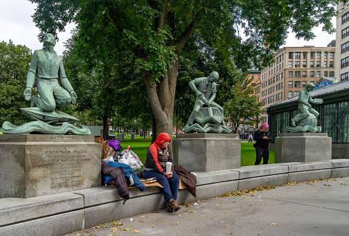 Homeless person sat beside statues in Boston Common at the beginning of the freedom trail.  Boston, Massachusetts, USA.
