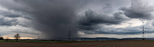istock Panoramic view of a thunderstorm moving over the Taunus with grey clouds, with ploughed and fallow fields in the foreground and a high-voltage overhead power line 1802149951