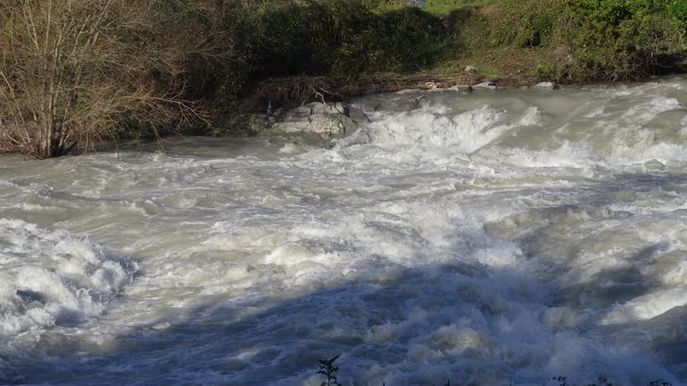 The river swollen after heavy rainfall and floodwater crashing through valley. The water flows fast from the high valley to the plain. General contest of a river in flood