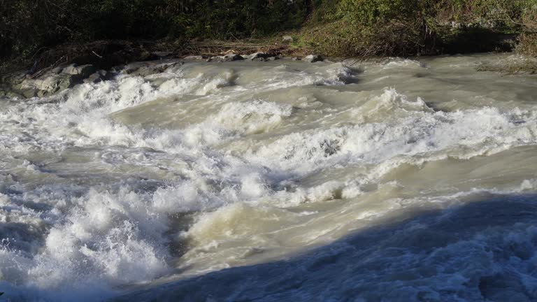 The river swollen after heavy rainfall and floodwater crashing through valley. The water flows fast from the high valley to the plain. General contest of a river in flood