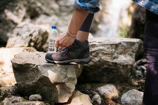 Close-up of a woman tying shoelaces standing on rocky mountain trail. Cropped shot of a female hiker tying hiking boots laces on a rock while on hiking trip.