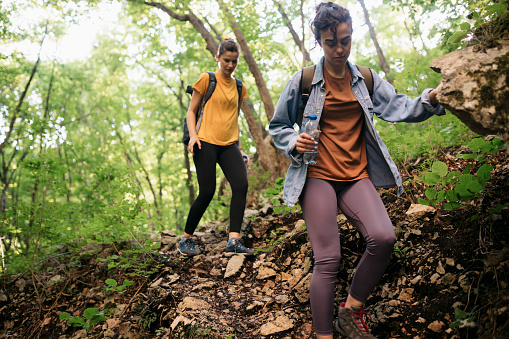 Two female hikers walking down mountain trail. Women friends travellers hiking down forest trail.