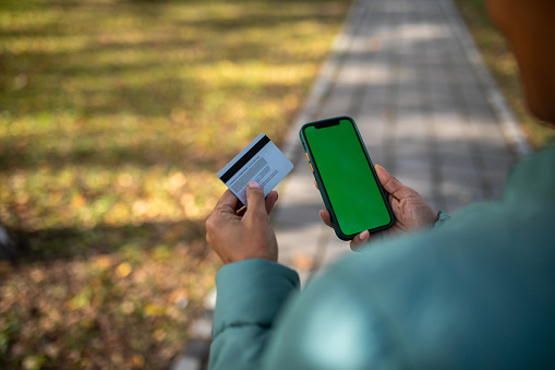 Over the shoulder view of woman holding phone with green screen and credit card in other hand