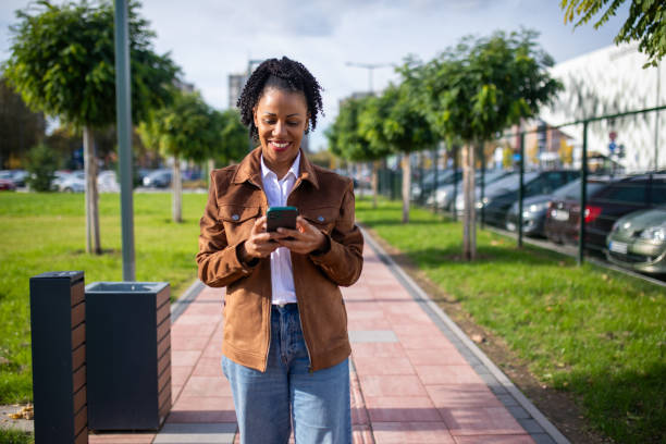 istock Beautiful smiling woman using smart phone on sunny day while walking in public park 1802247159