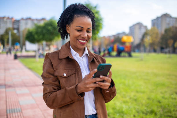 istock Beautiful smiling woman using smart phone on sunny day while walking in public park 1802247448