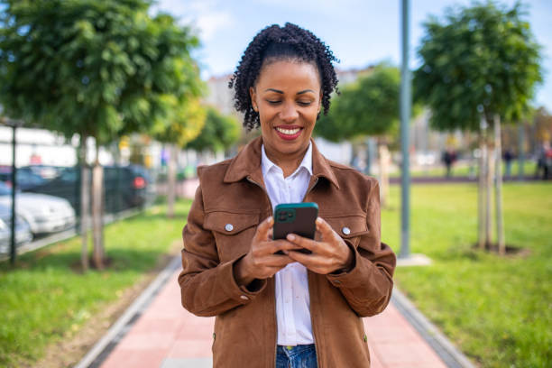 istock Beautiful smiling woman using smart phone on sunny day while walking in public park 1802247459