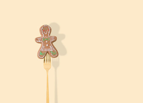 Gingerbread Christmas tree decoration pricked on a fork on pastel beige background. New Year party background. Minimal style. Creative Christmas or New Year concept. Winter holidays idea.