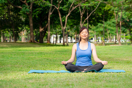 A pleasure woman closed eyes sitting on yoga matt doing yoga in the nature park among the morning sunshine