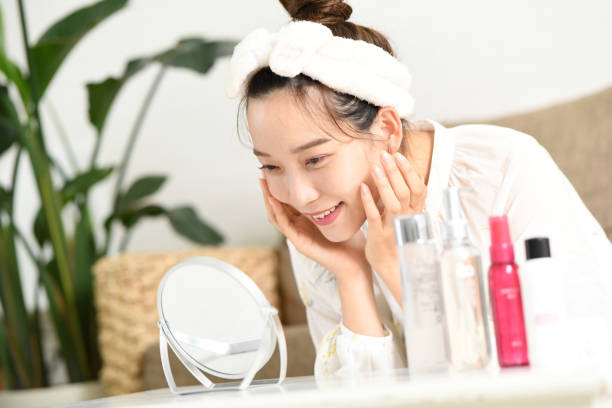 Asian woman in loungewear doing skin care while looking in the mirror Asian woman in loungewear doing skin care while looking in the mirror