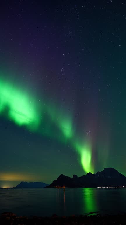 Vibrant and colorful aurora rising from a distant mountain during late blue hour.